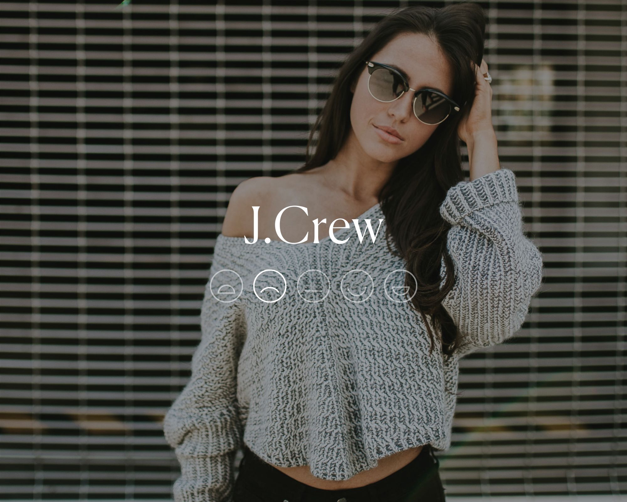 A grey knitted sweater with white text overlaid reading J.Crew above a highlighted sad emoji face.