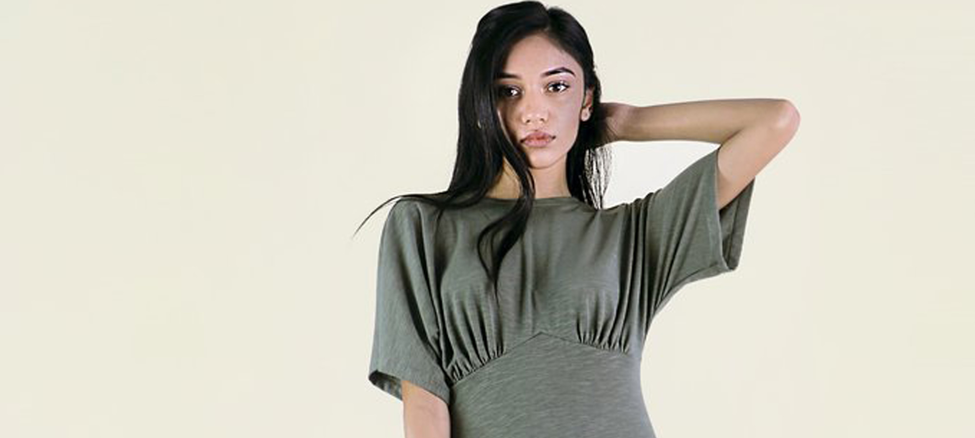 A woman in a grey/green dress touches her hair.