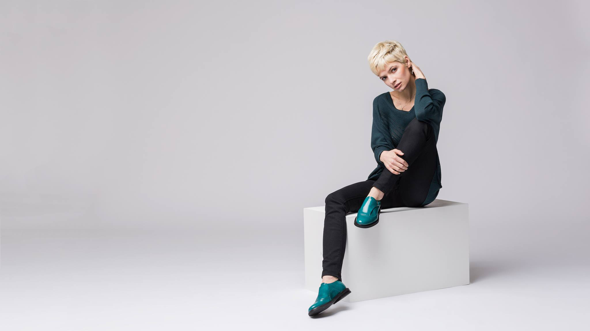 A woman with green patent brogues sits on a white box.