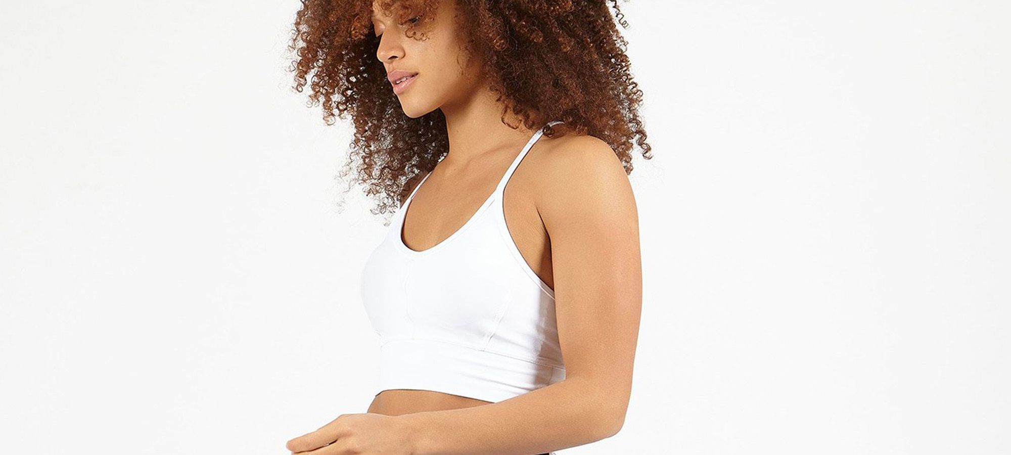 A woman with dark curl hair wear a white yoga crop top.