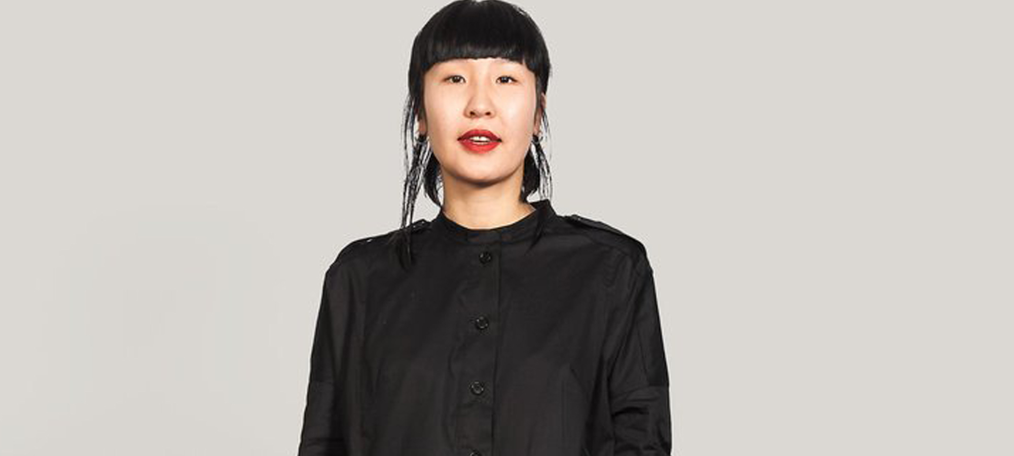 A woman wears a black shirt dress and red lipstick.