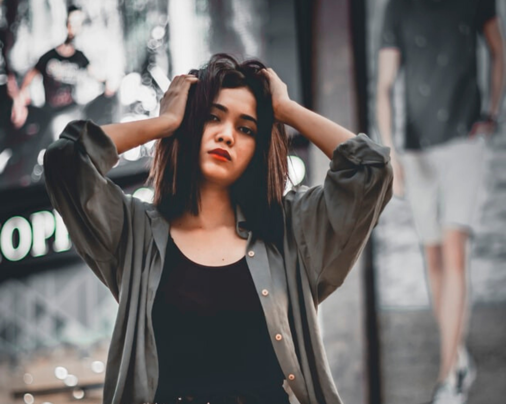 asian woman holding head in grey unbuttoned shirt