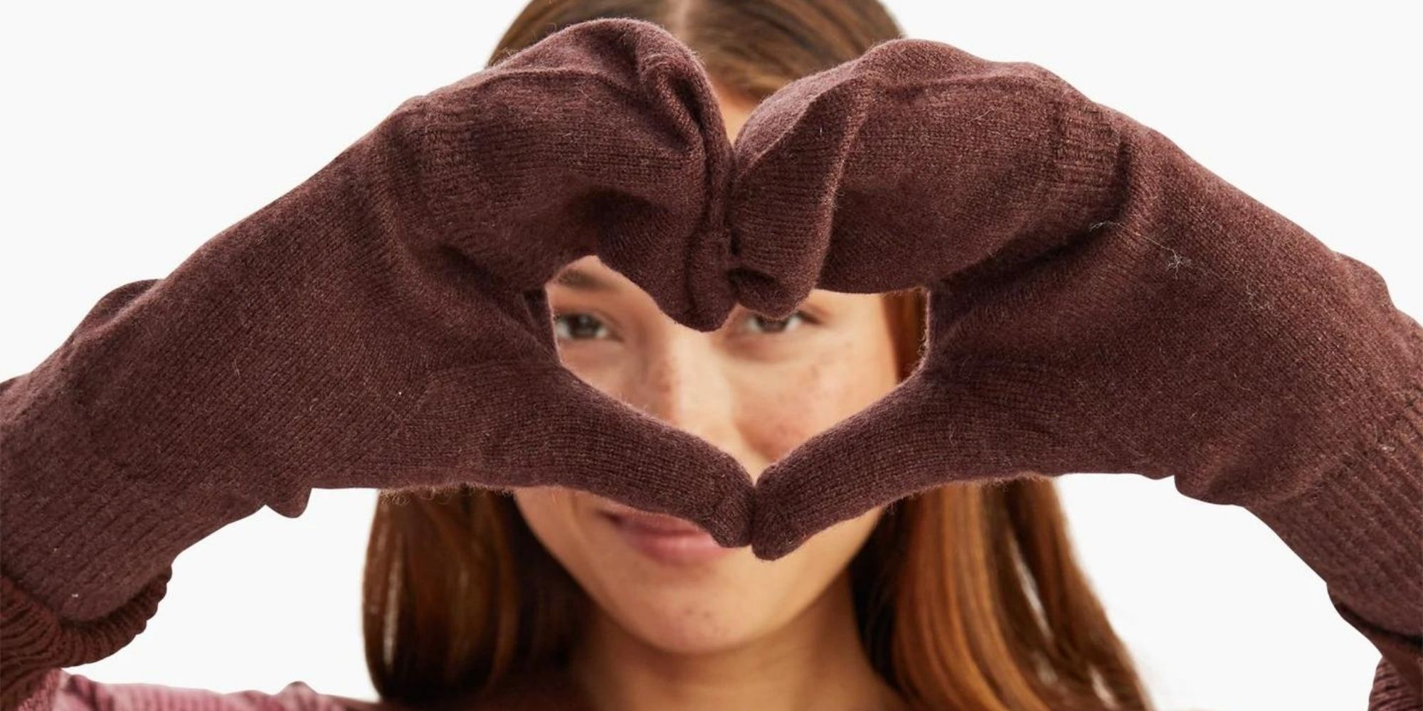 Someone making a love heart shape with their hands, wearing brown cashmere gloves by NAADAM.