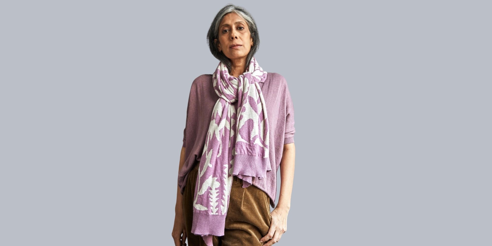 An older person wearing a pink and white orchid print organic cotton scarf by No Nasties.