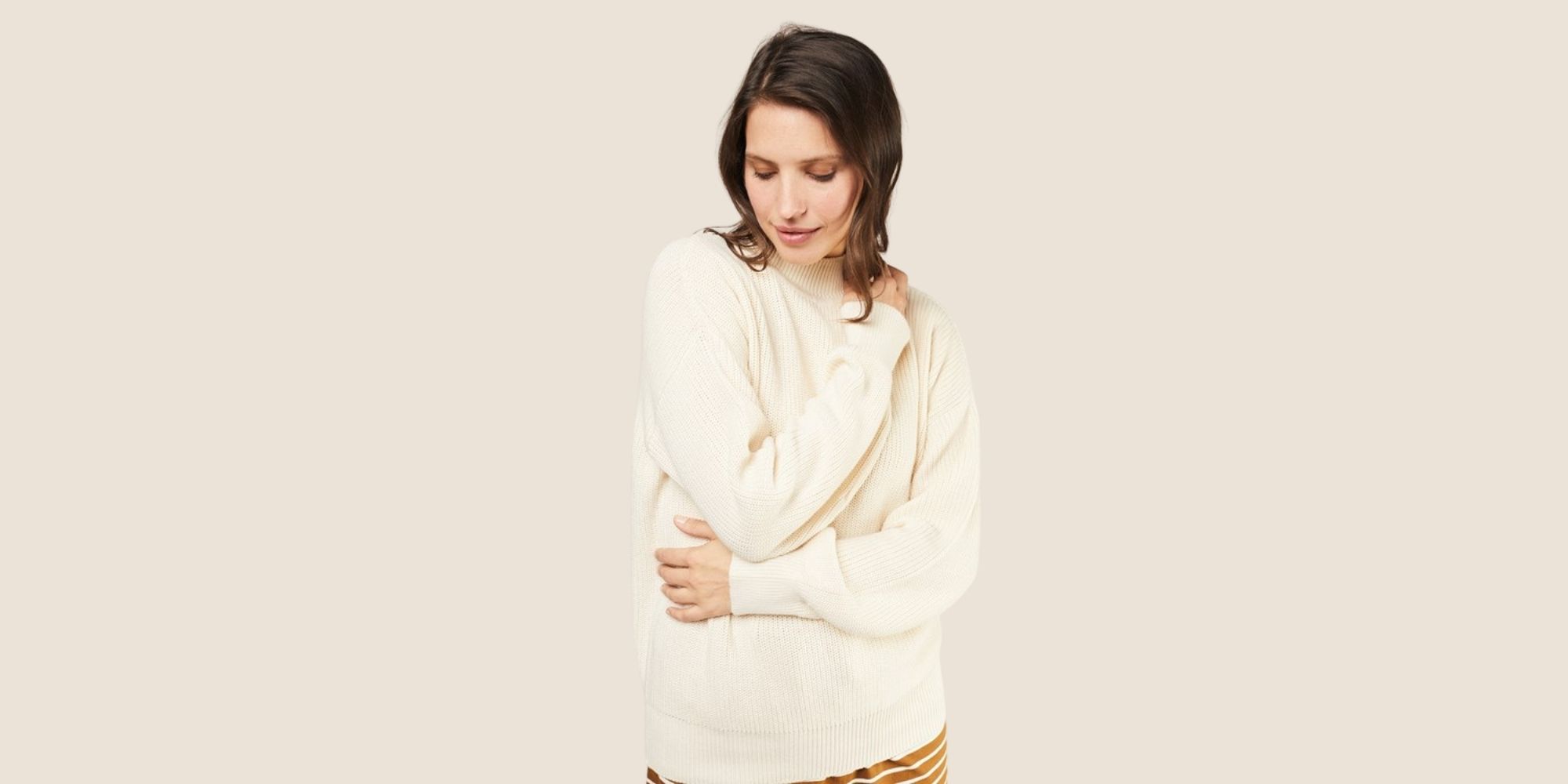 Someone hugging themselves while wearing a People Tree cream organic cotton sustainable winter essential jumper.