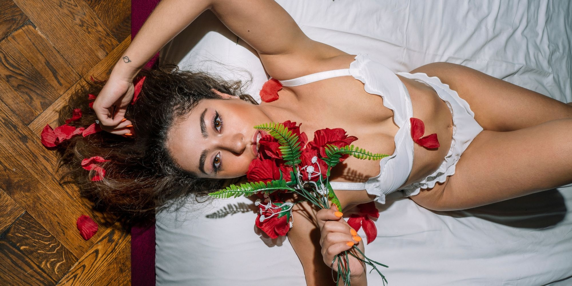 Someone reclining surrounded by red roses in white frilled bra and underwear by Colieco.