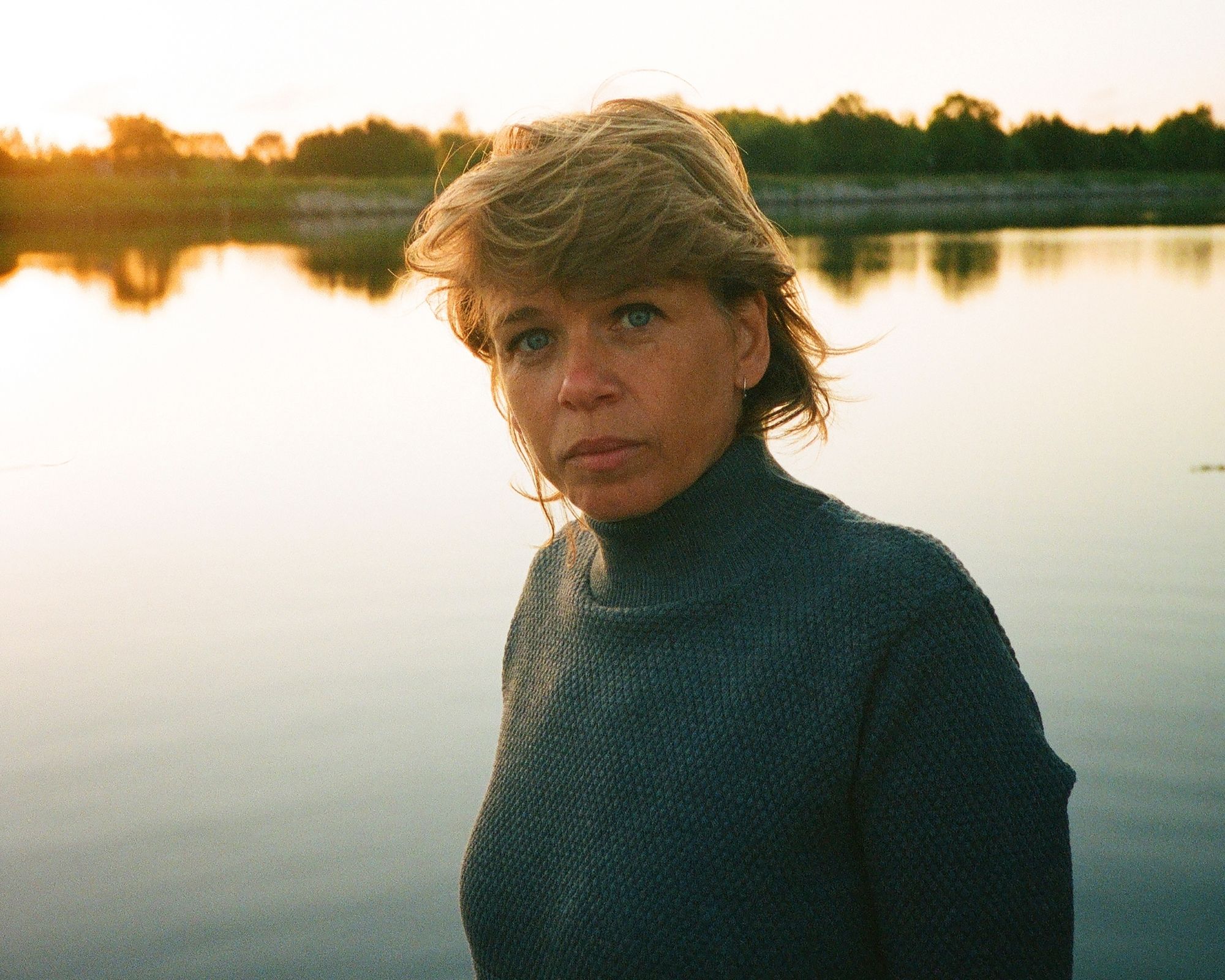 woman standing in front of a lake wearing sustainable knitwear by Le Pirol