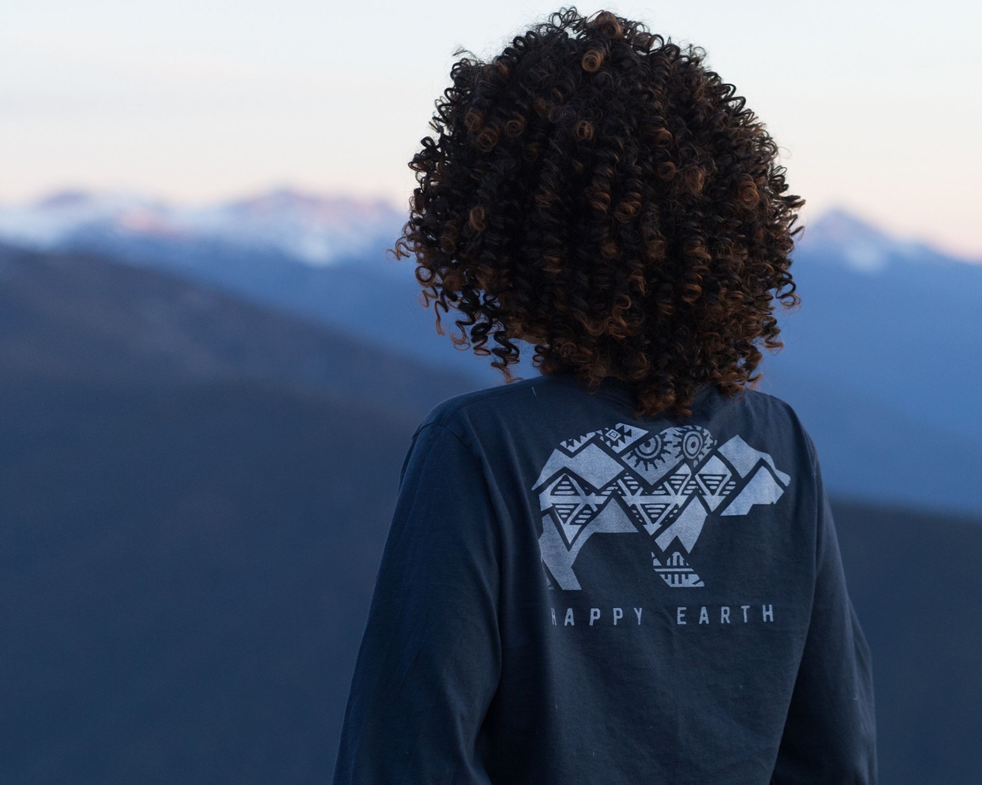 woman of colour wearing sustainable long sleeve blue graphic tee by Happy Earth looking over mountains