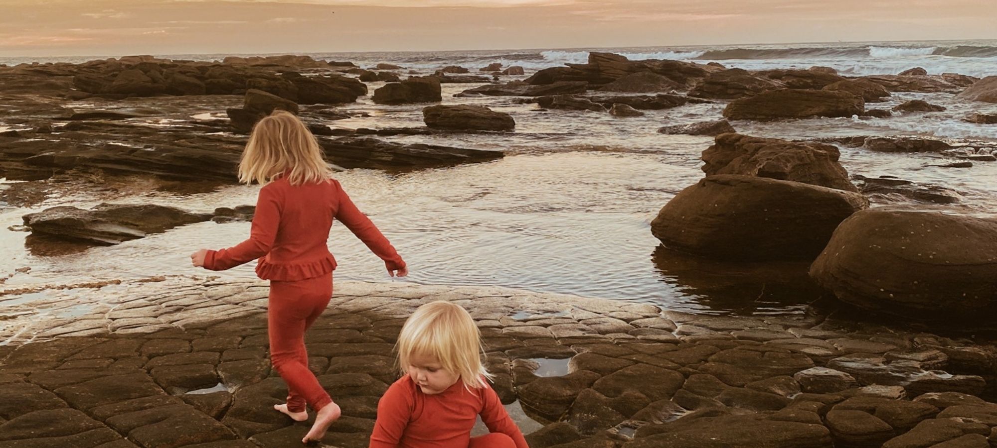 two blonde toddlers wearing bright orange sustainable baby clothes by Zuzu & co