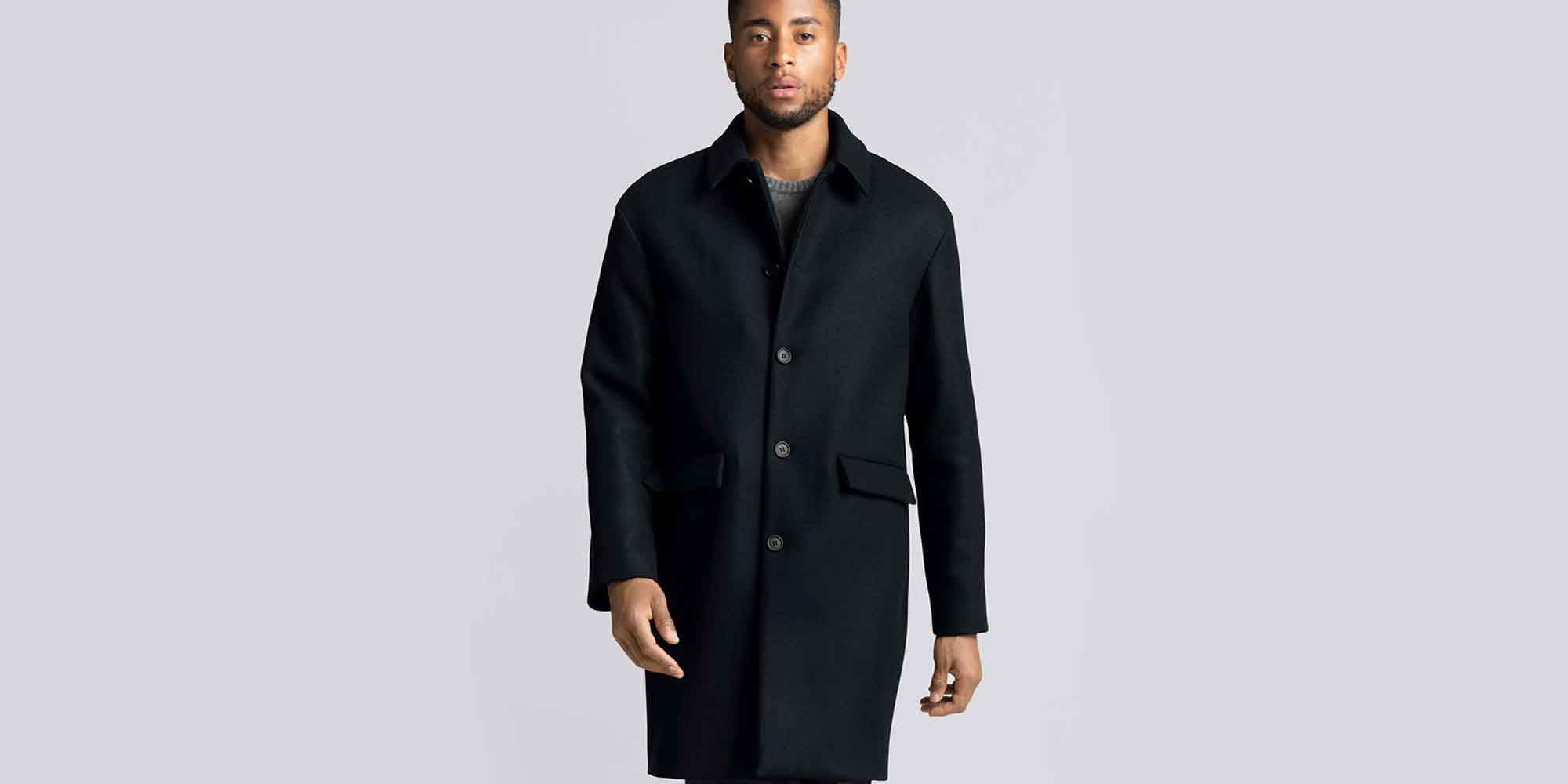 man of colour wearing black sustainable wardrobe essentials including trench coat by ASKET