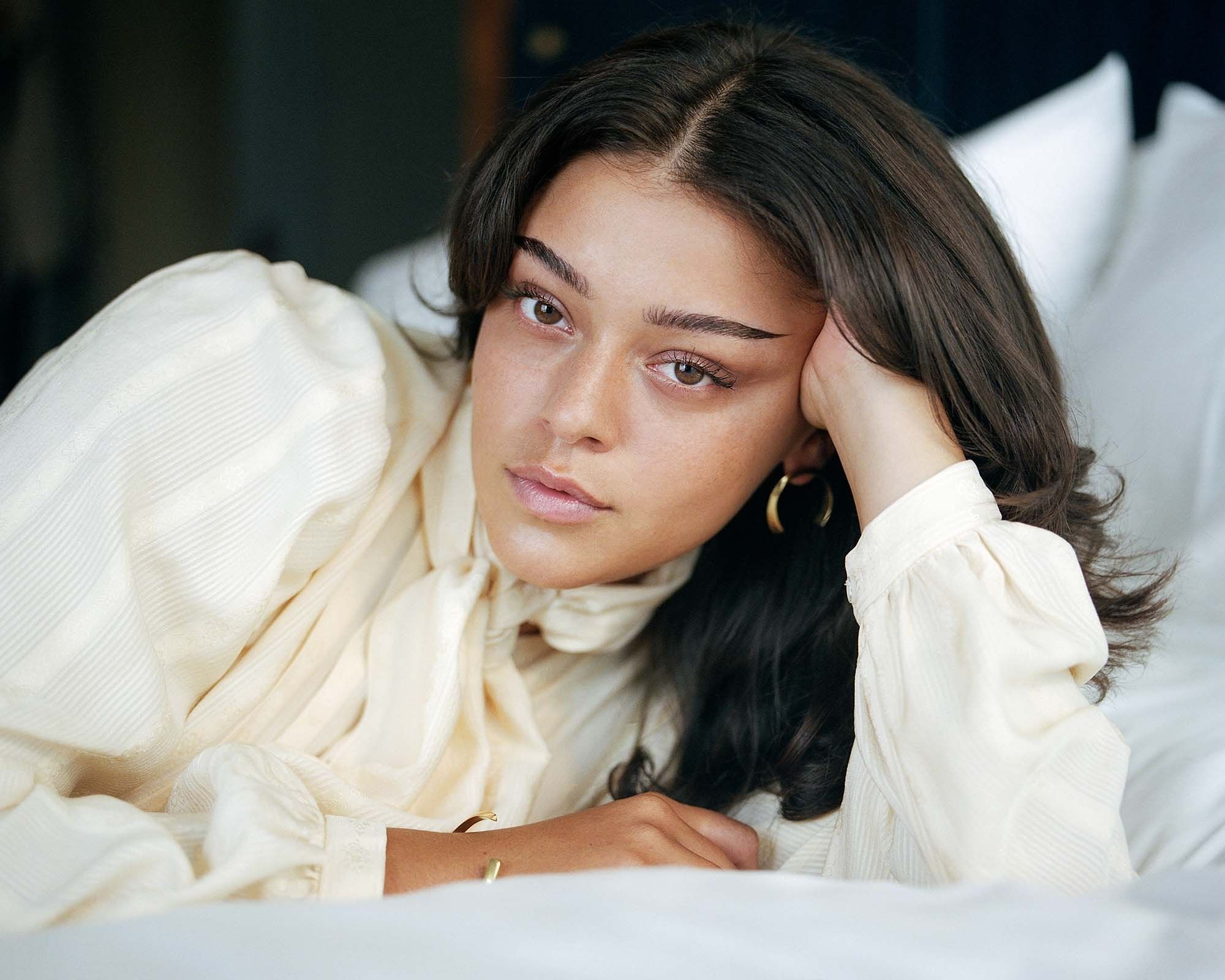 woman reclining on bed wearing sustainable jewellery by Raven + Lily
