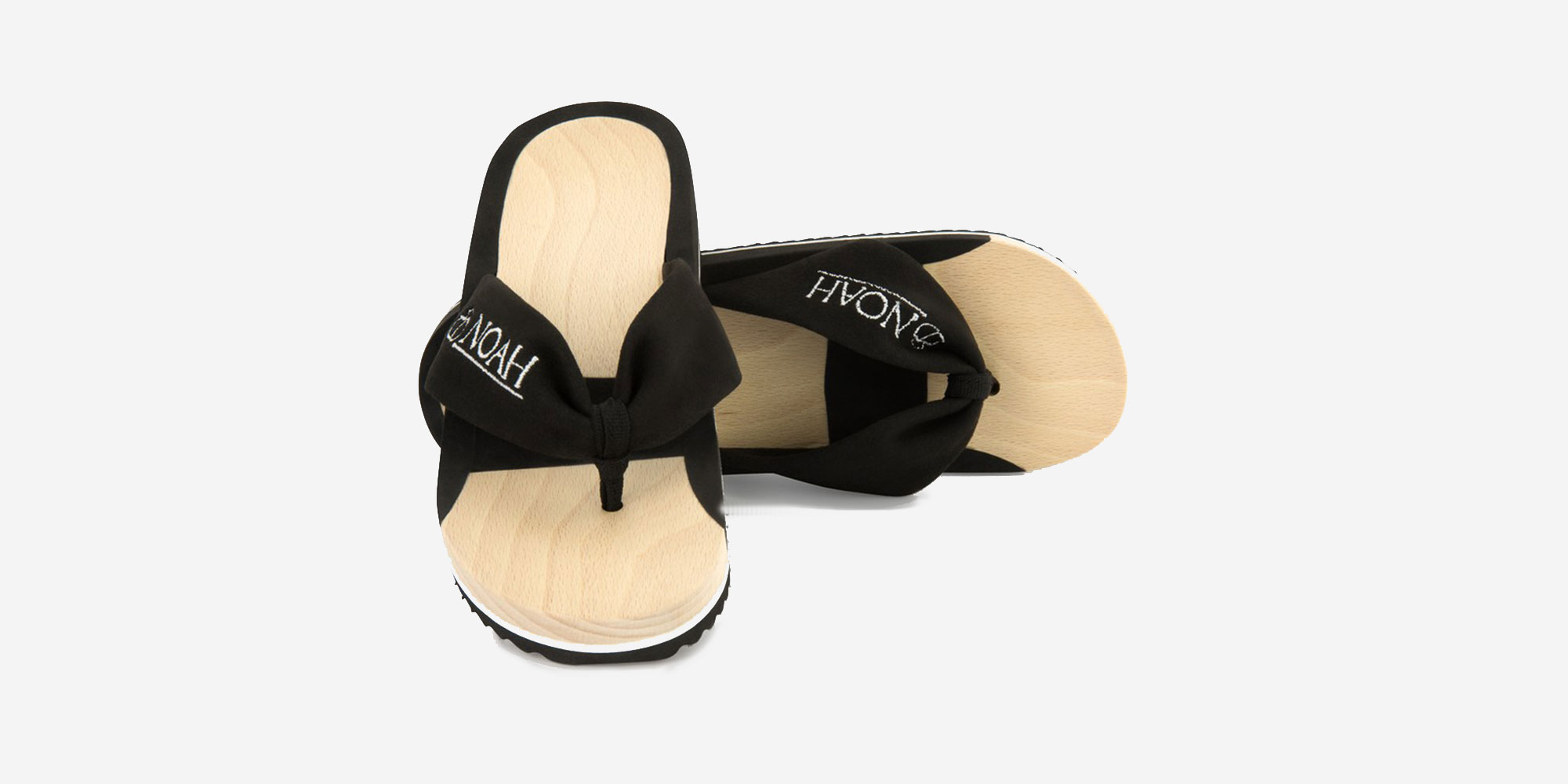 A pair of wooden flip flops with thick black thong-style banding with the brand name