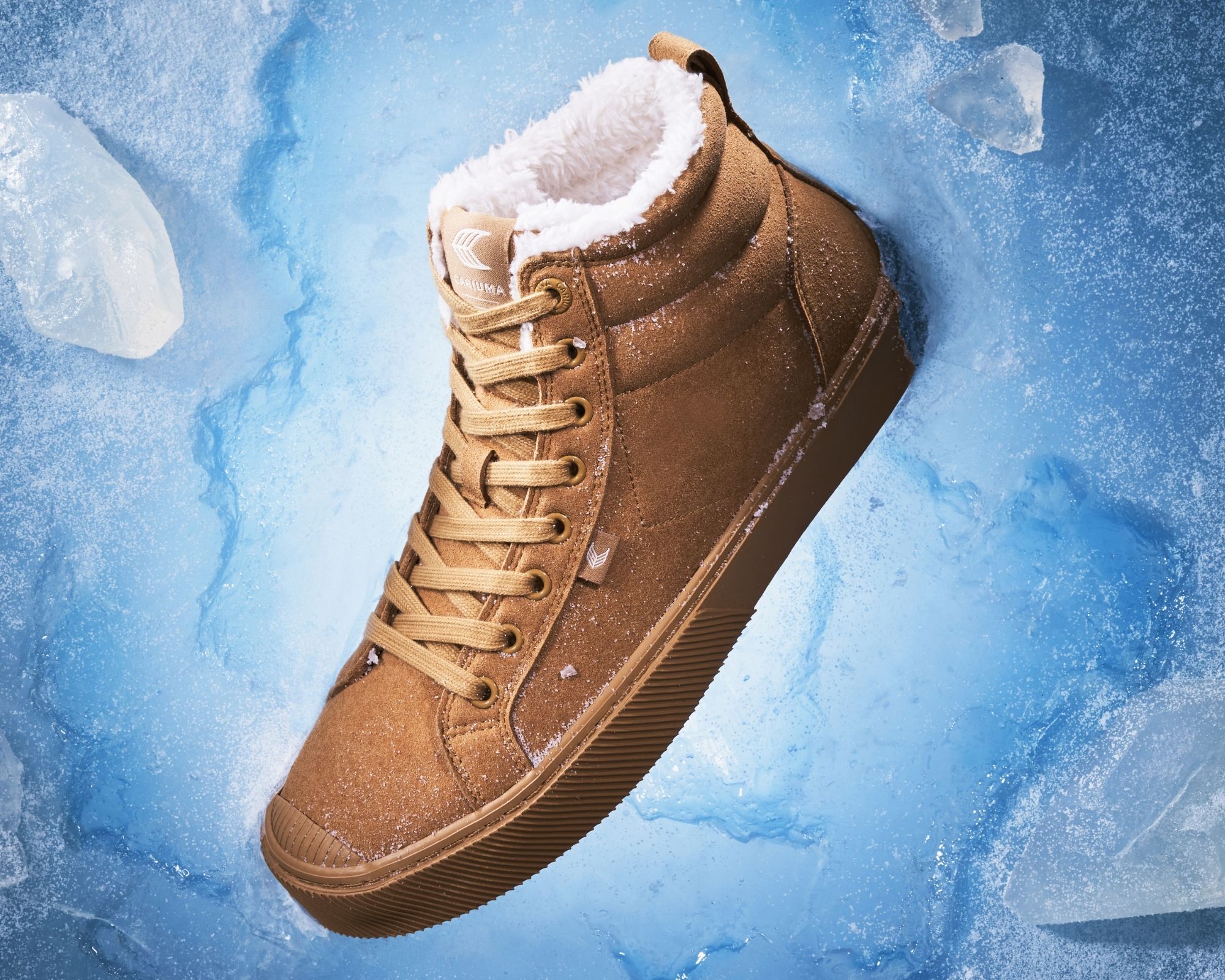 An all camel sustainable vegan winter boot sticking out of a wall of ice by the heel.