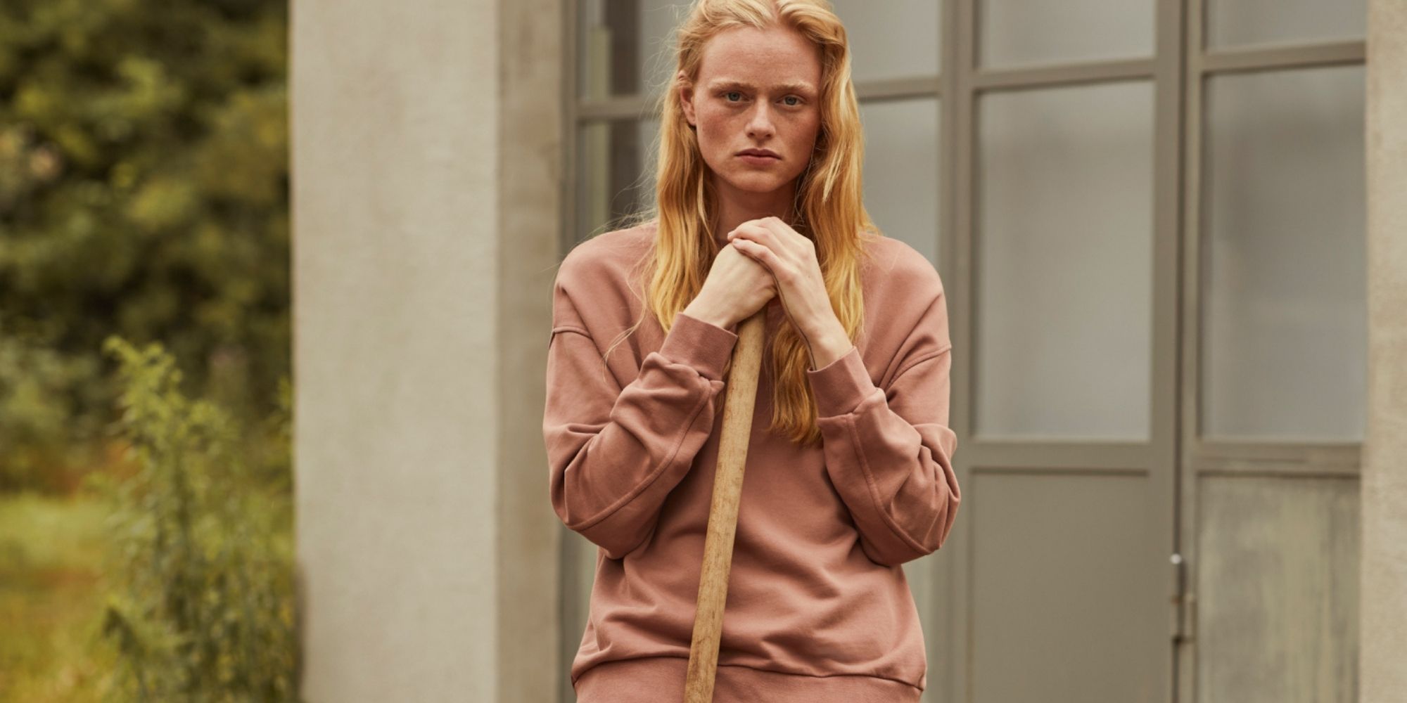Someone wearing a naturally dyed pink sweatsuit by Armedangels and holding a garden tool.