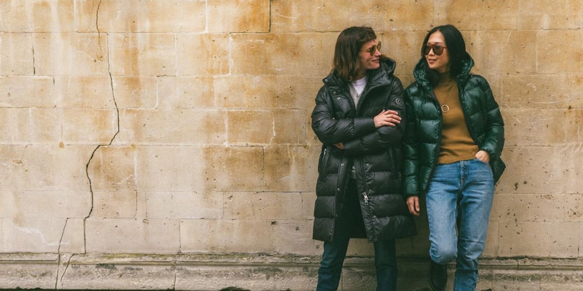 Two people leaning against a wall wearing black sustainable vegan puffer jackets by Culthread.