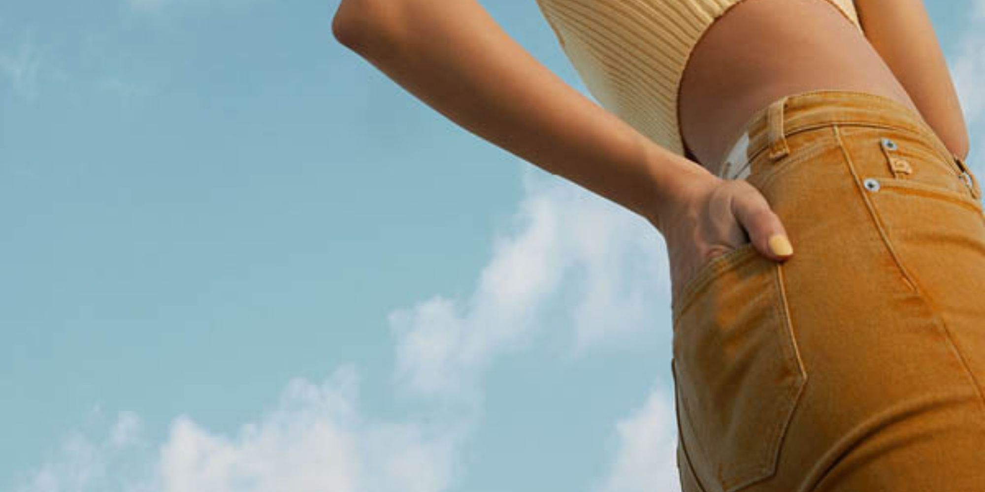 Cropped shot of someone with their hand in the back jeans pocket of orange naturally dyed jeans by MUD Jeans.