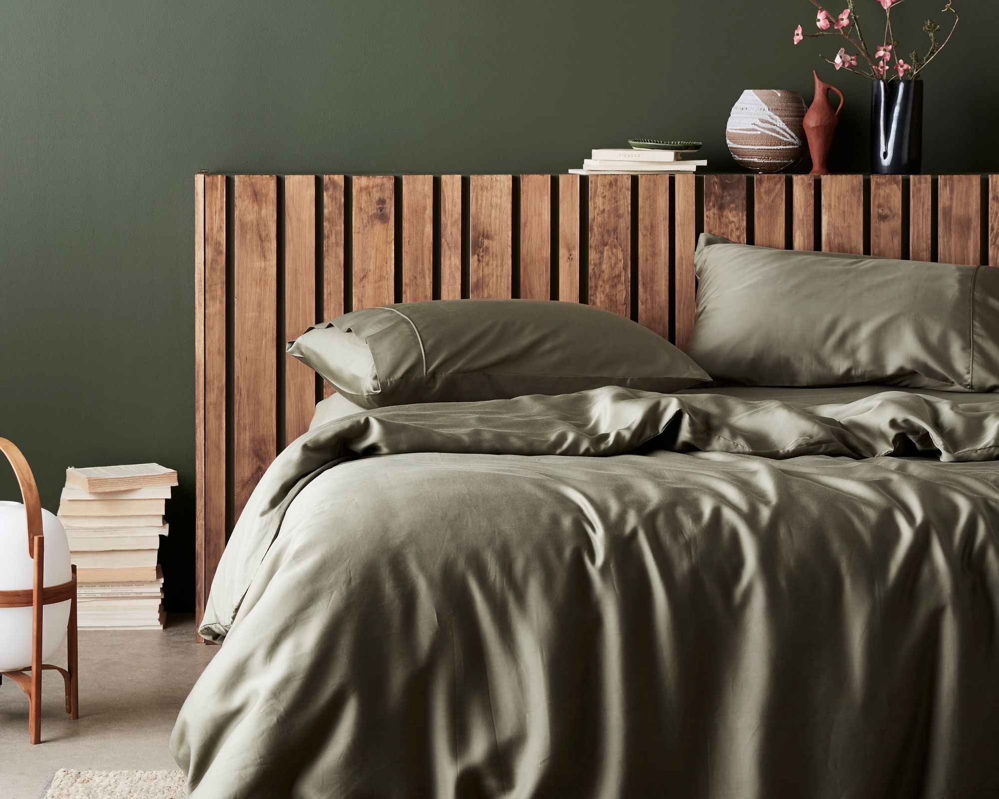 Cropped shot of moss green sustainable sheets by ettitude on a bed with a simple wooden frame.