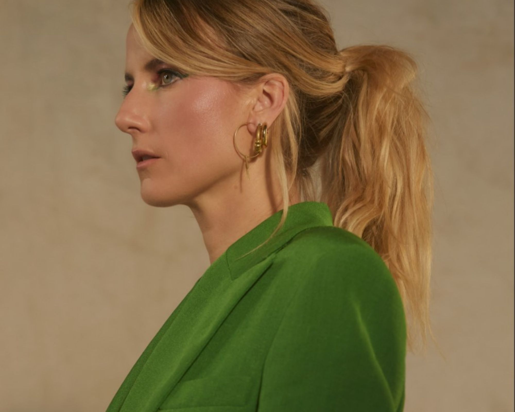 Profile studio shot of celebrity sustainable stylist Laura Sophie Cox wearing golden earrings designed in collaboration with ARTICLE22, paired with a green blazer.