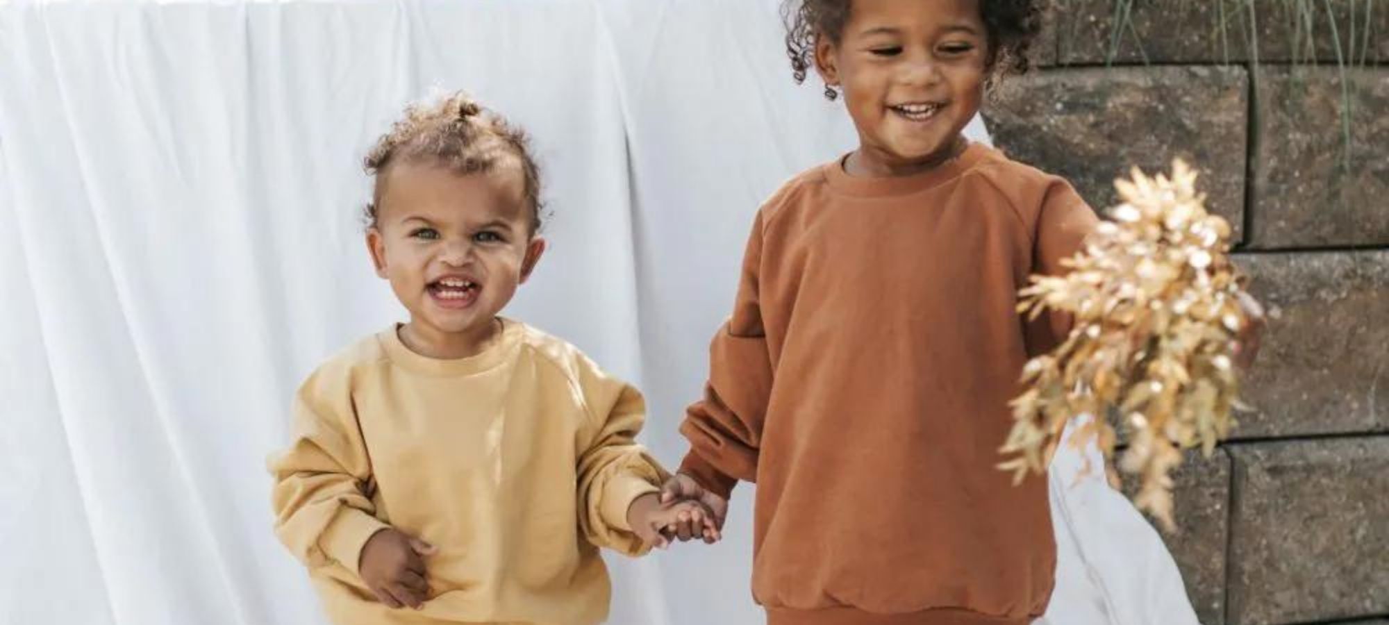 Two toddlers wearing neutral matching sweatsuits by Orbasics.