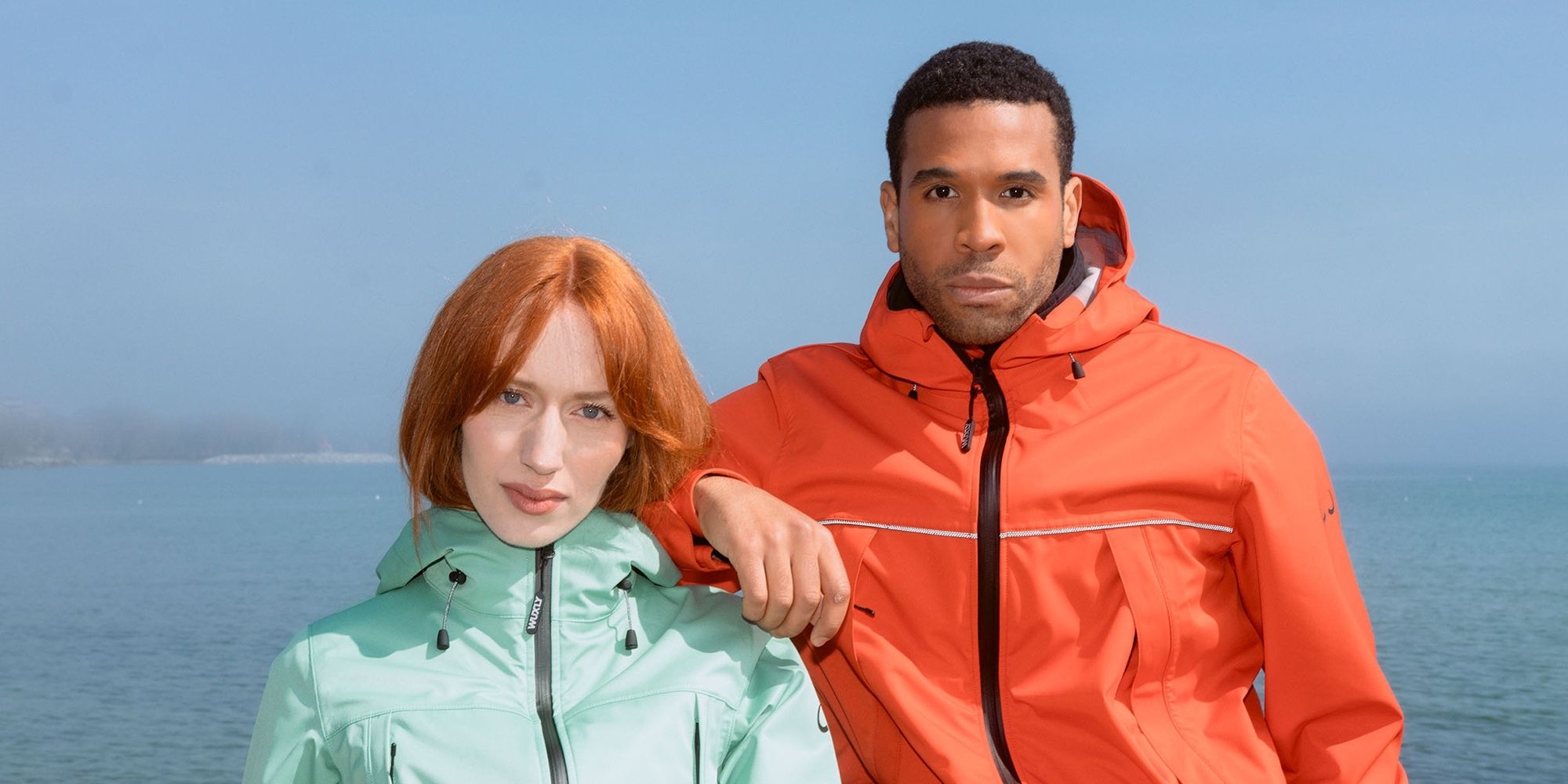 Two people outside wearing a mint green and a bright orange technical raincoat ethically made by Wuxly Movement.