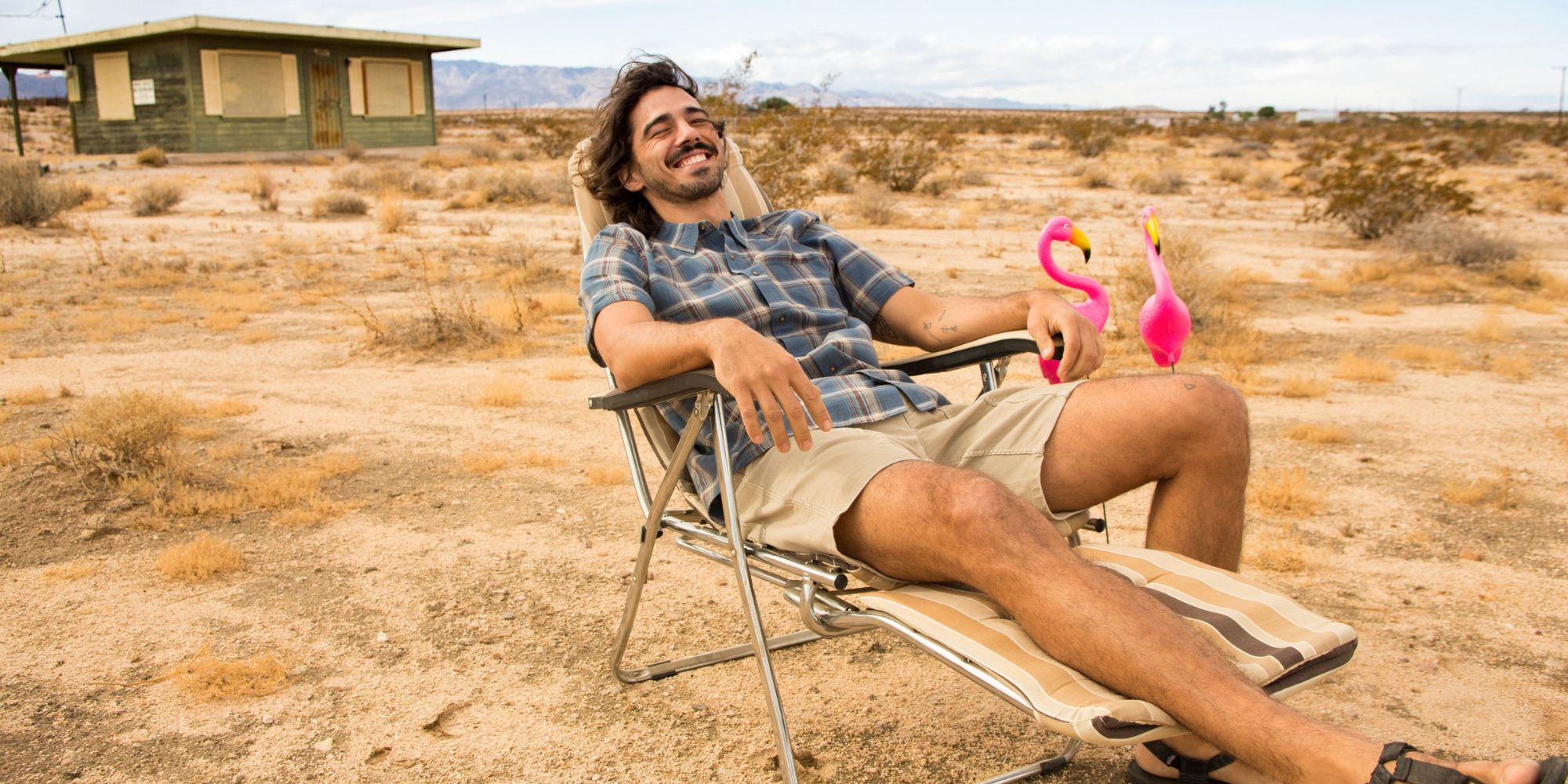 A happy looking person wearing Toad&Co shirt and shorts and reclining outdoors.