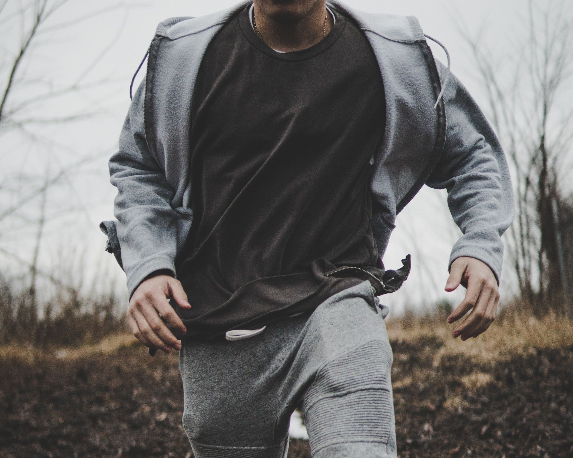 Someone wearing a grey tracksuit and black tee, running outdoors.