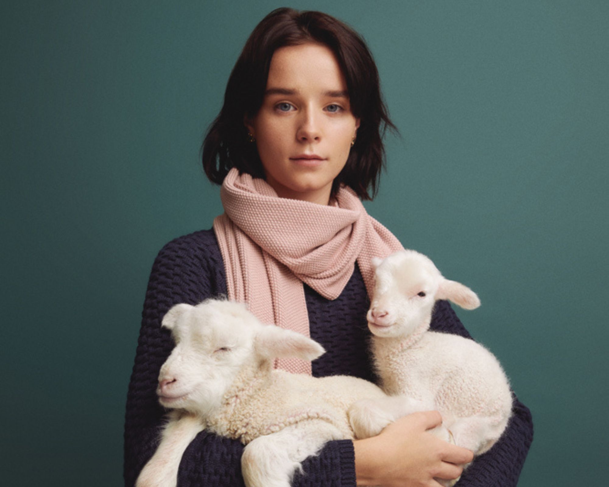 Author Emma Hakansson wearing a vegan wool alternative sweater and holding two lambs in her arms.