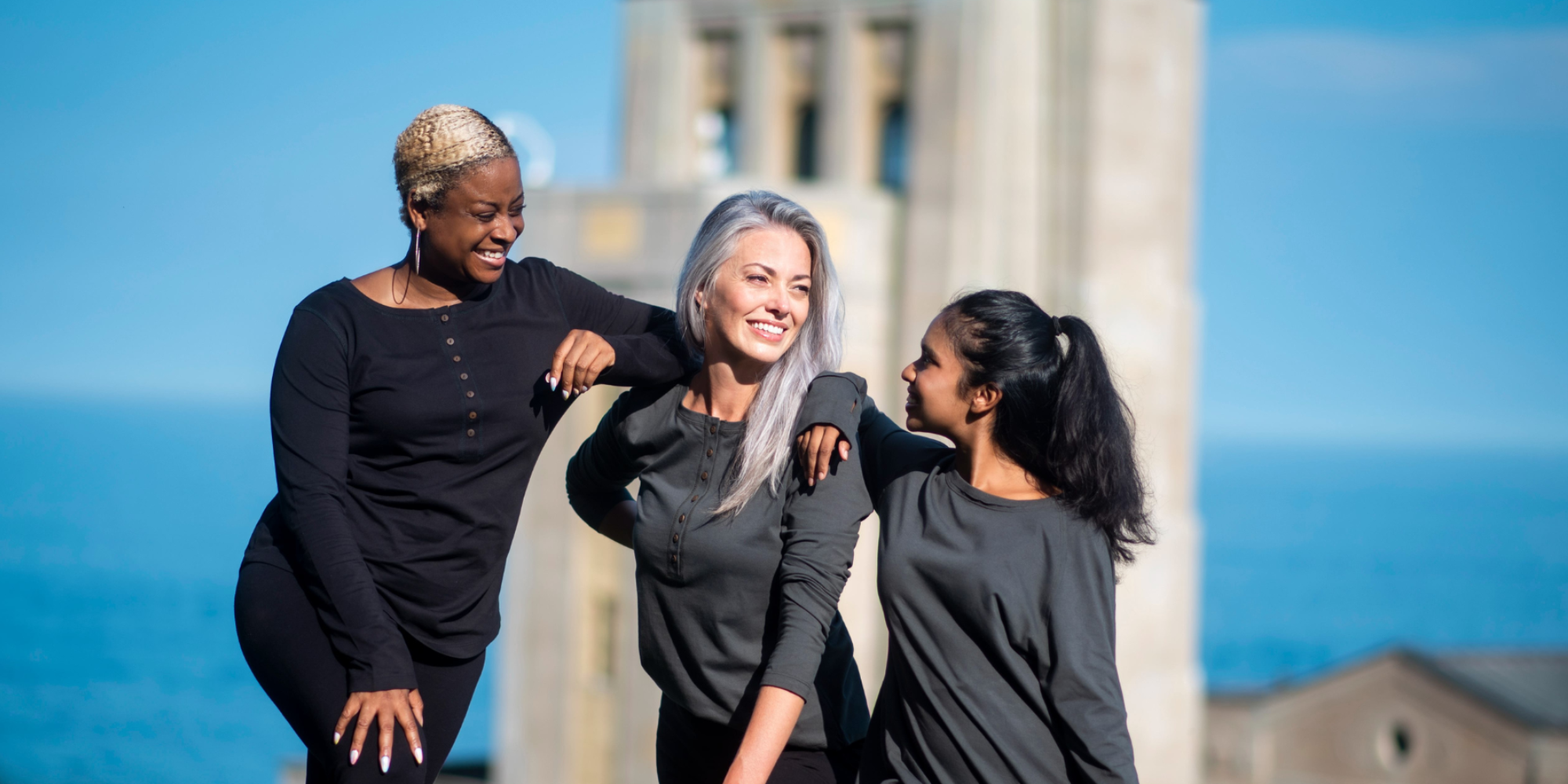 three people standing by the sea in long-sleeved grey and black Fair Trade Organic tops by The Good Tee