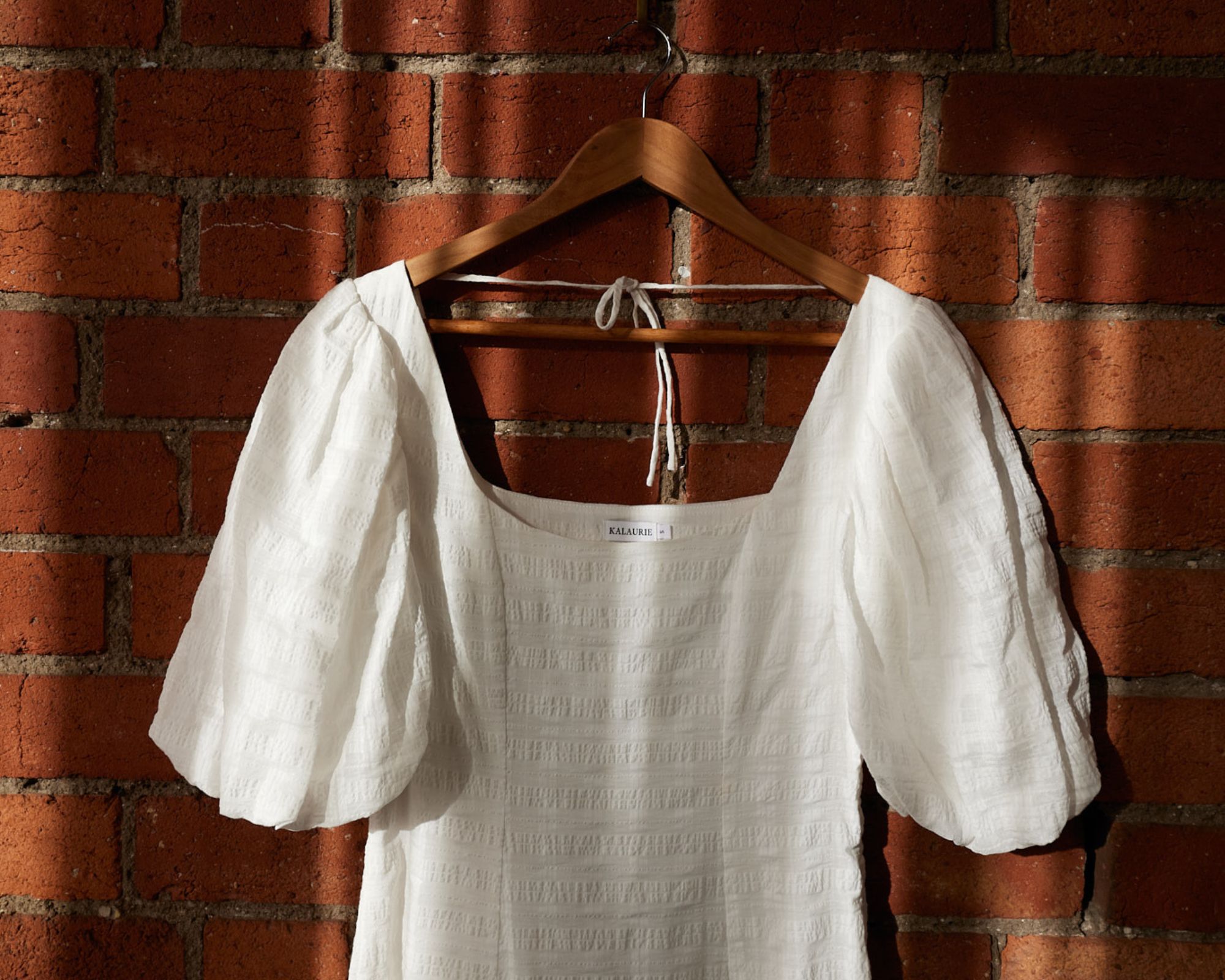 A white handmade puff sleeve dress hanging on a clothes hanger by Kalaurie.