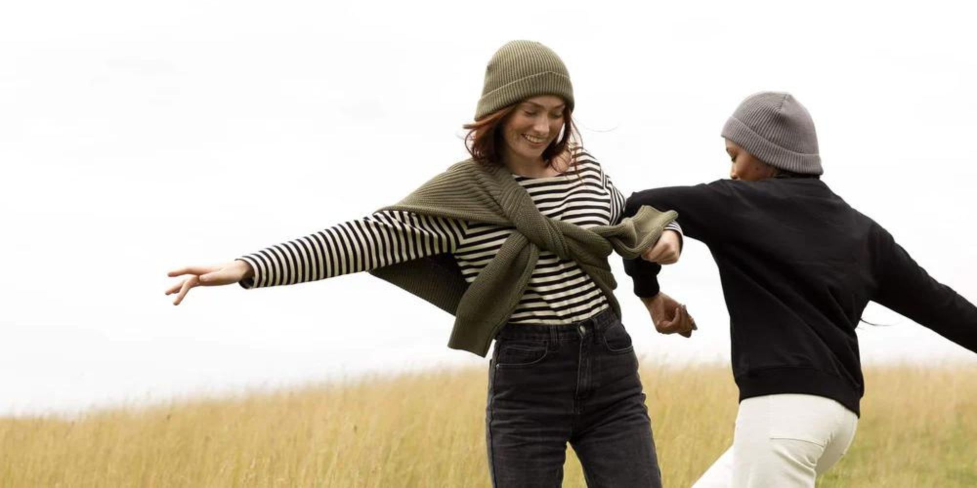 Two people outside with linked arms, wearing sweaters and beanies by The SUSS Edit.