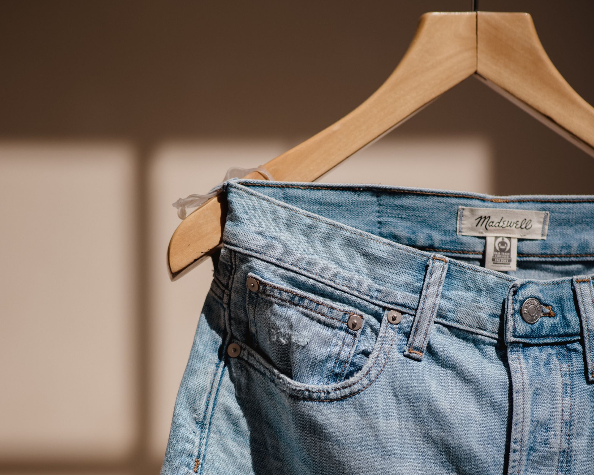 A pair of jeans on a wooden hanger.