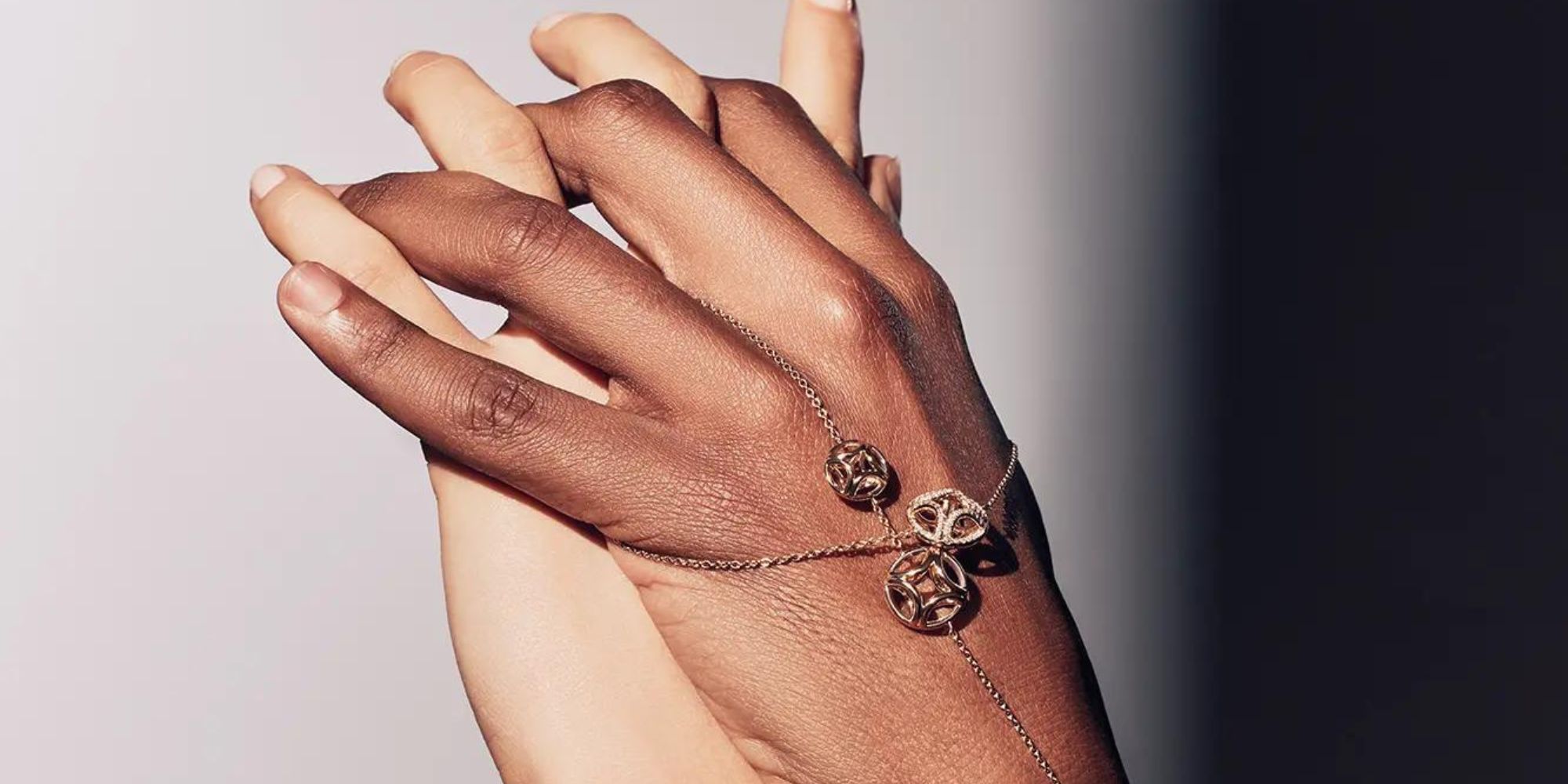 Two hands clasping, the one on top wears fine chain jewellery from Loyal E. Paris.