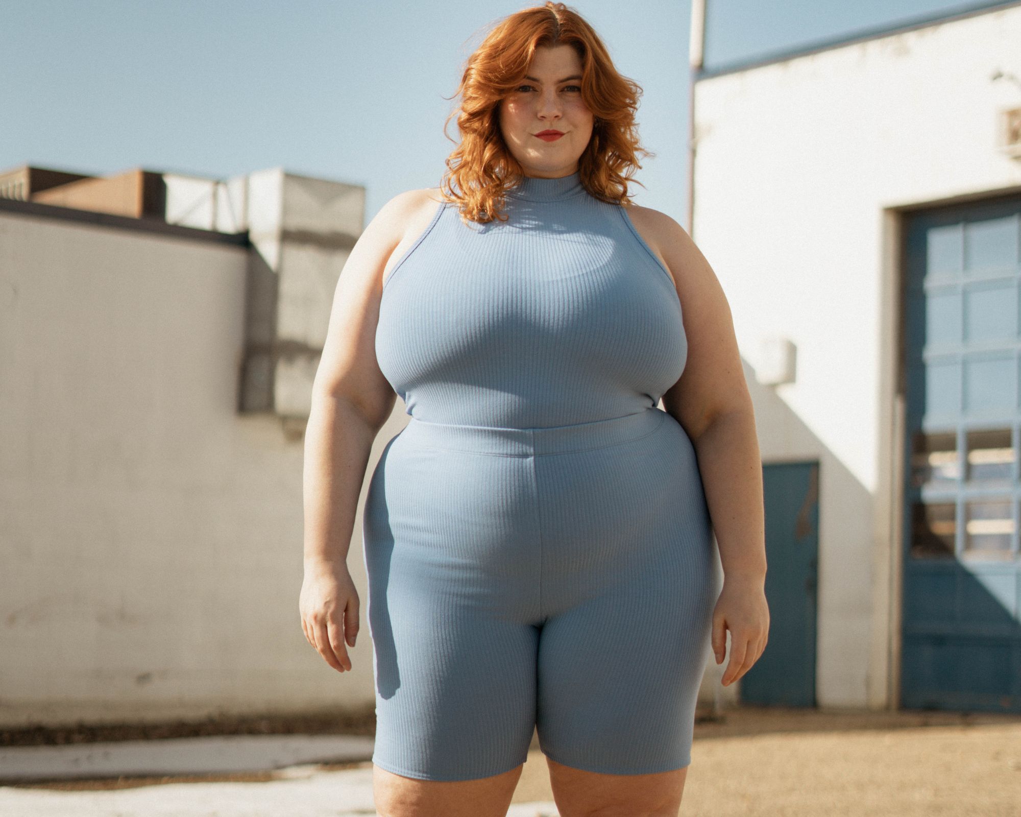 Plus-size influencer Marielle Elizabeth standing on a rooftop wearing a powder blue activewear set with a determined look on her face.