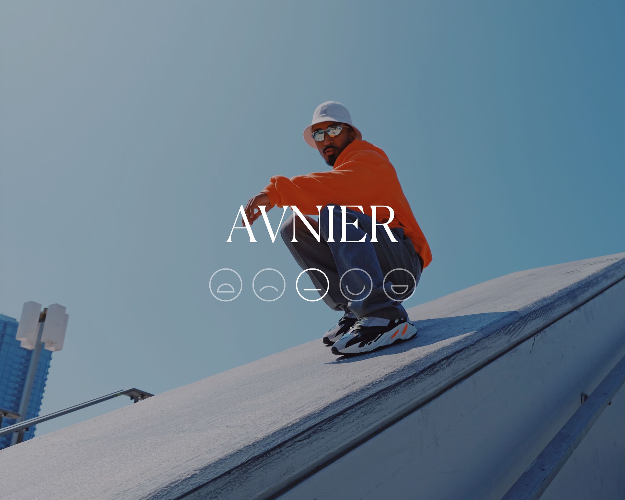 Someone crouching on a wall wearing a red hoodie in a streetwear style outfit, with font saying AVNIER overlaid above a neutral emoji face.