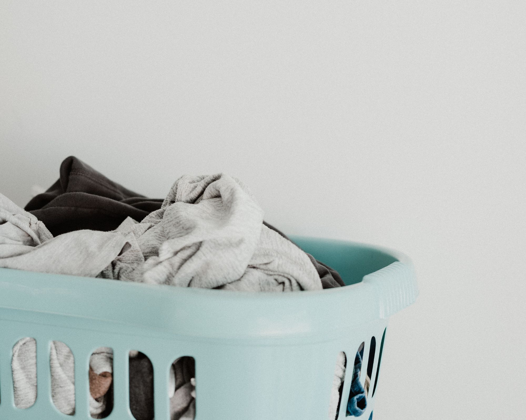A pile of dirty clothing in a light blue laundry basket.