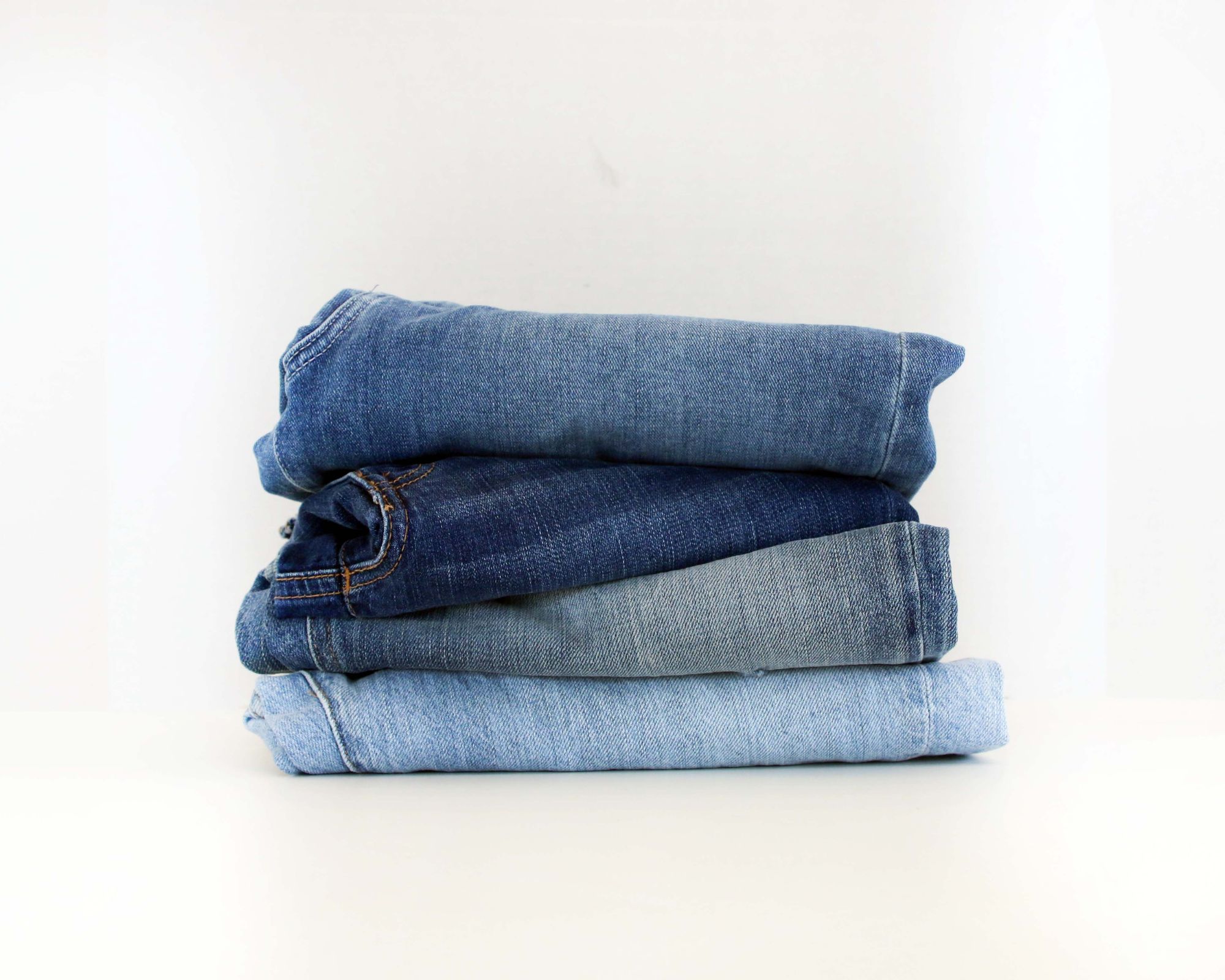 A pile of four denim jeans in different shades folded neatly in a stack.