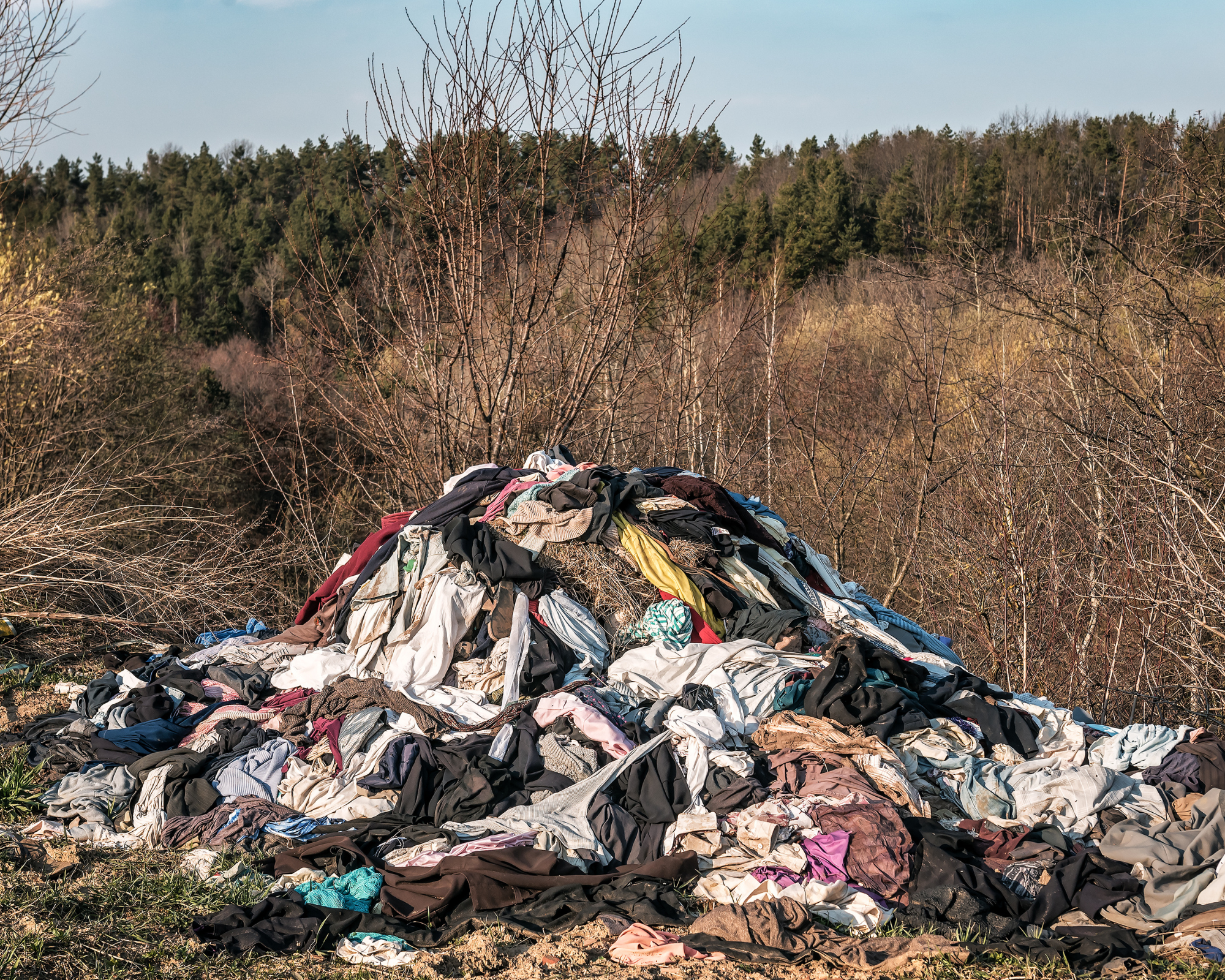 A pile of wasted clothes towers in a generic forest