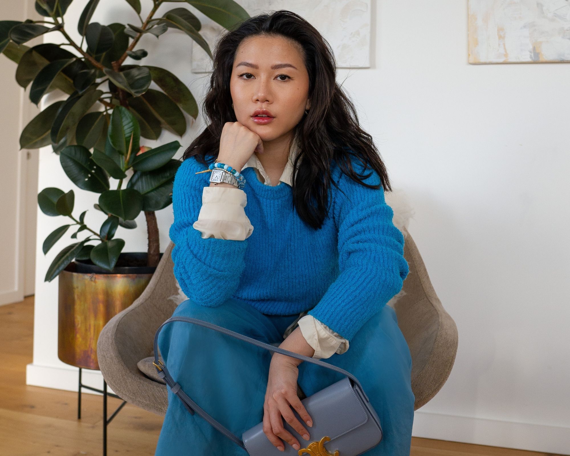 Author Andrea Cheong wears a bright blue jumper and leans forward confidently in her chair, her chin resting on her fist.