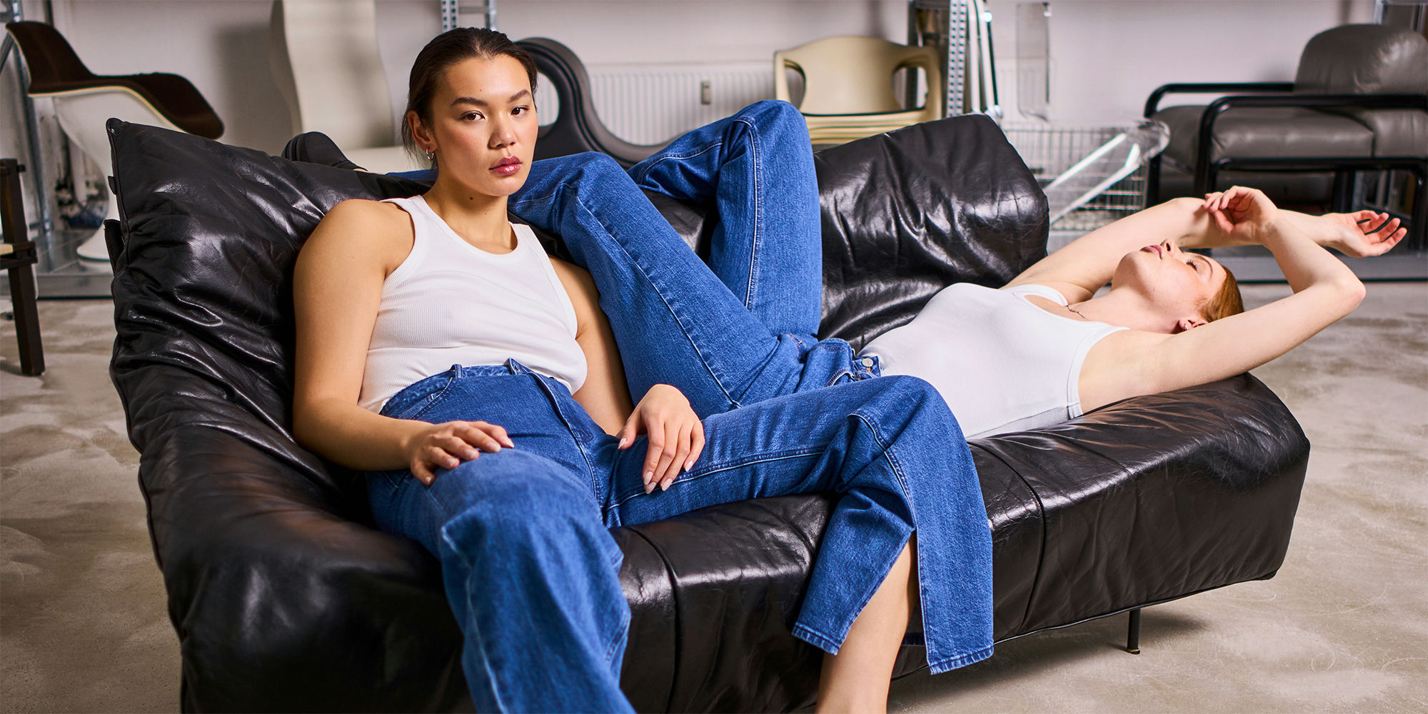 Two people reclining on a couch wearing mid wash lower-impact denim jeans made collaboratively by DAWN Denim and JAN 'N JUNE.