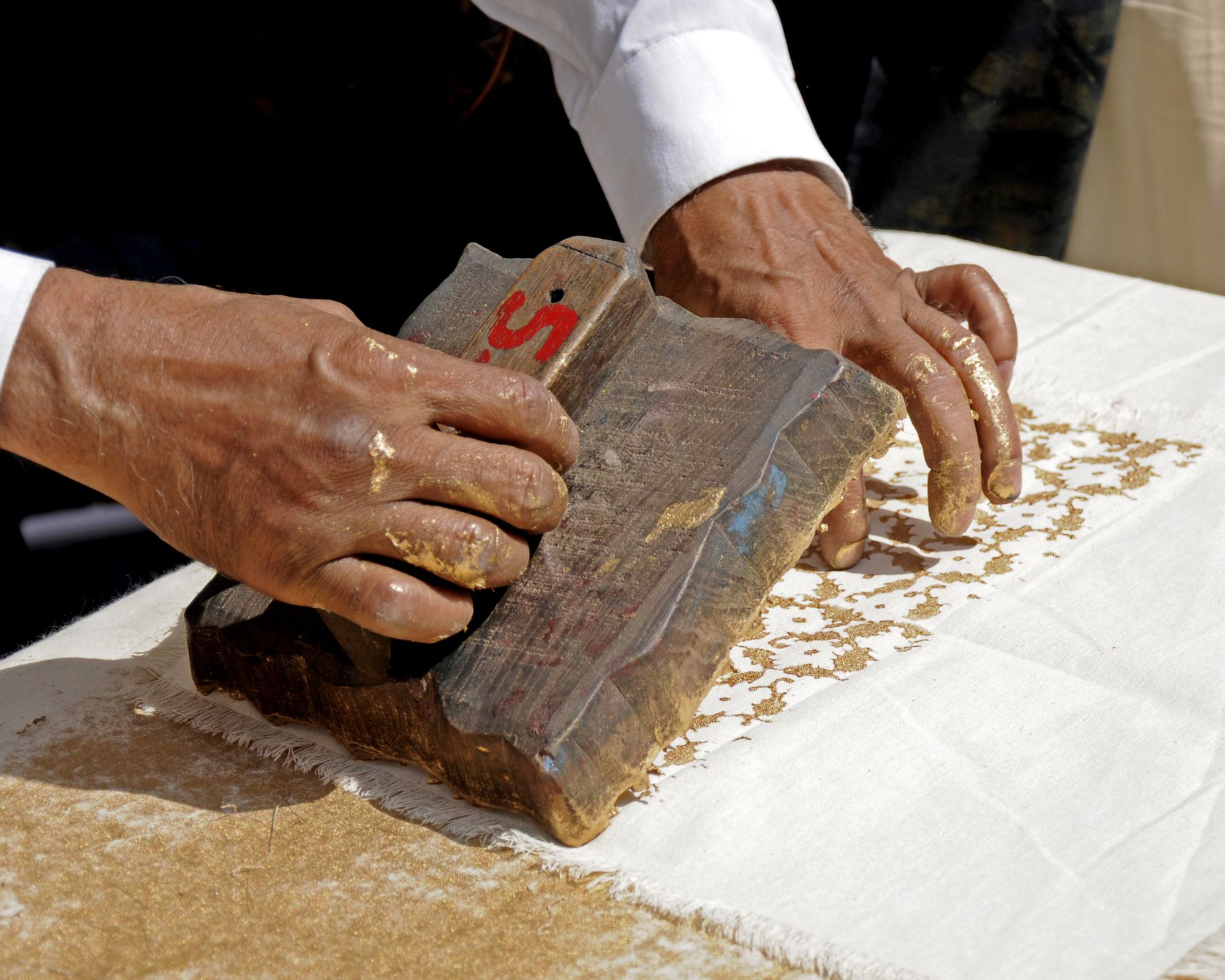 A close up of someone's hands block printing white fabric in a brown tone.