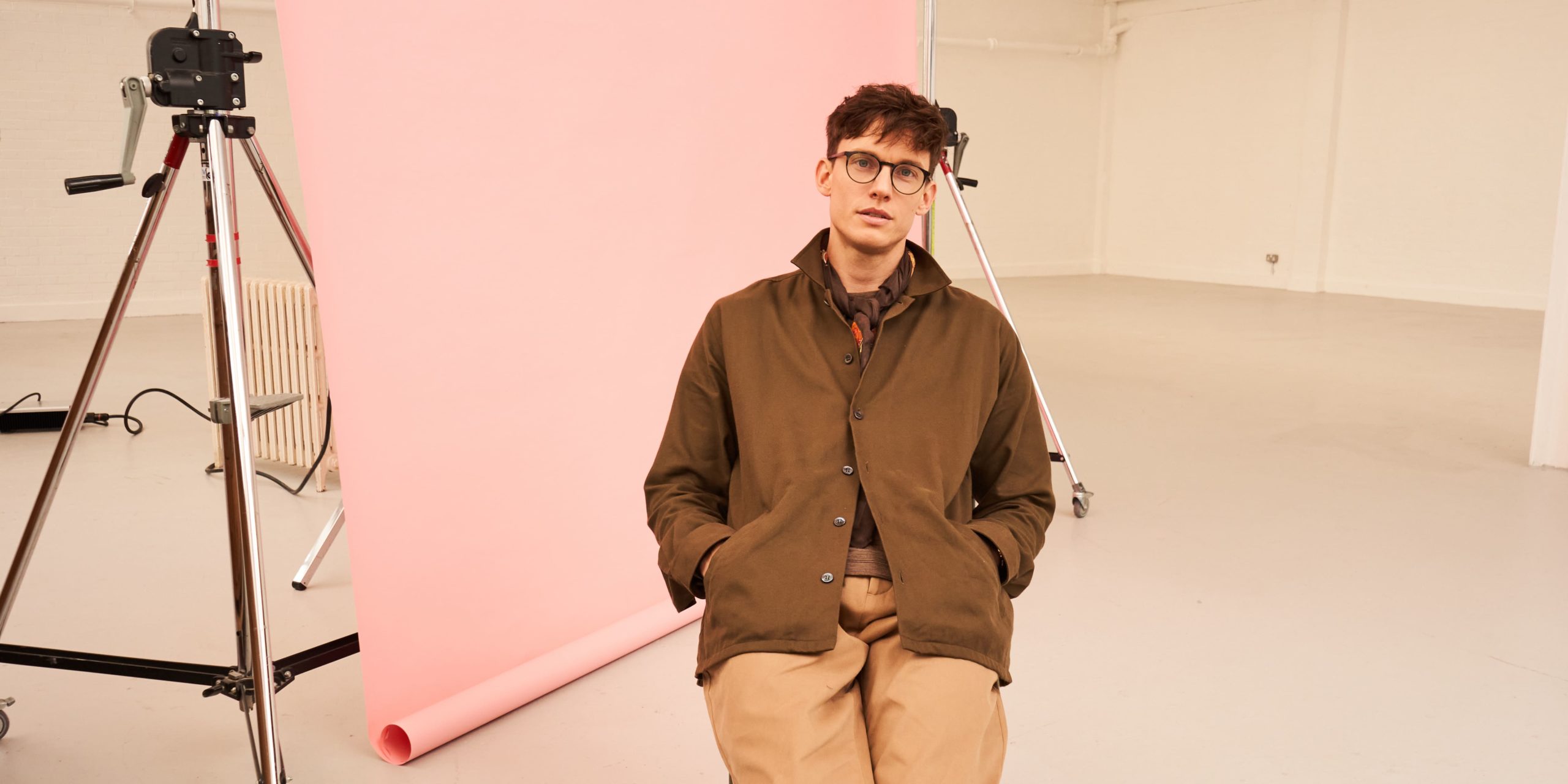 Male presenting person sitting on a chair wearing jacket and long pants