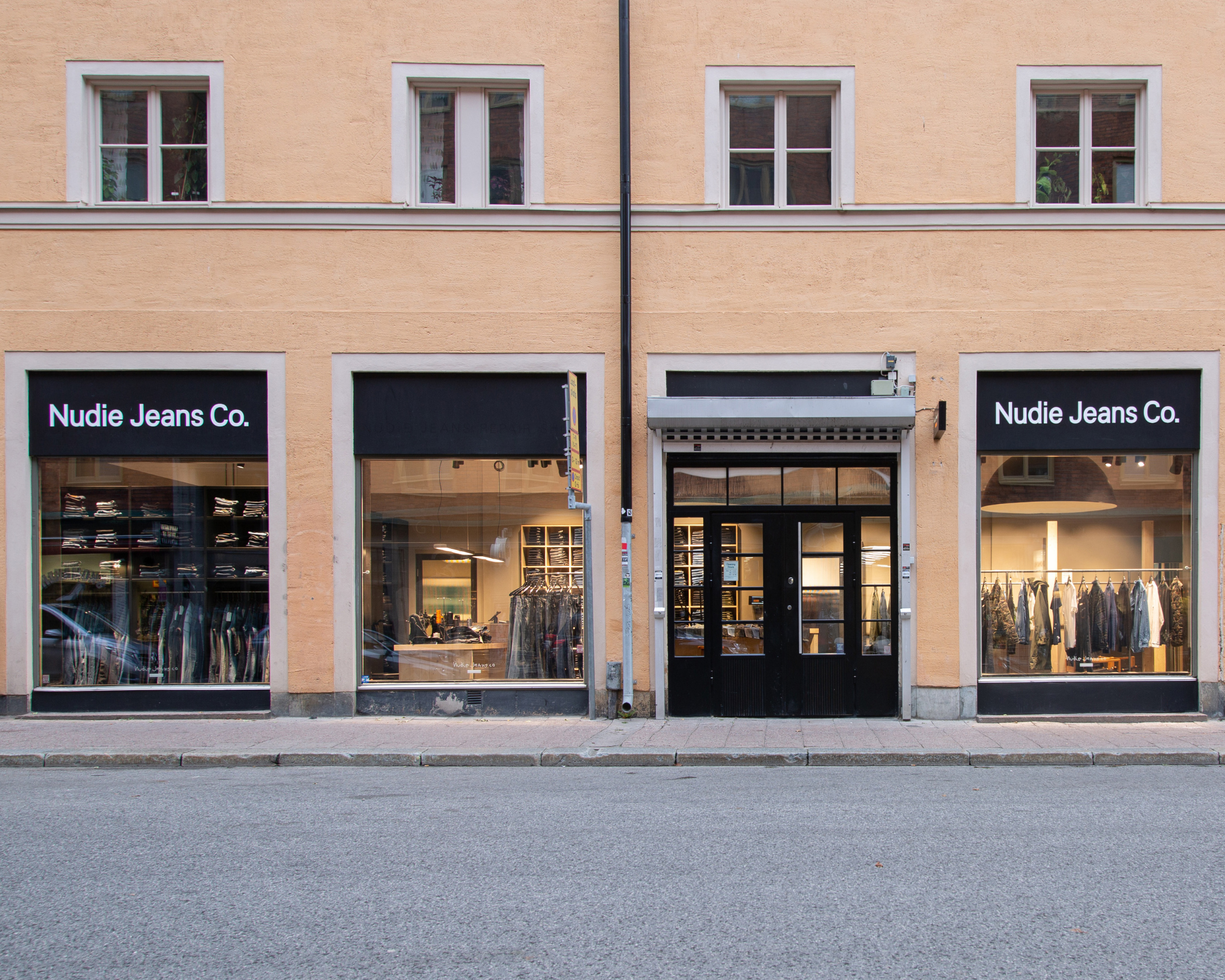 Street view of a Nudie Jeans Repair Shop, showing its premium denim hanging in the window and a repair station inside
